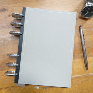 A picture of a discbound planner on a table with a pen and watch. Part of an article - sustainable planning: create an eco - friendly planner [discbound]