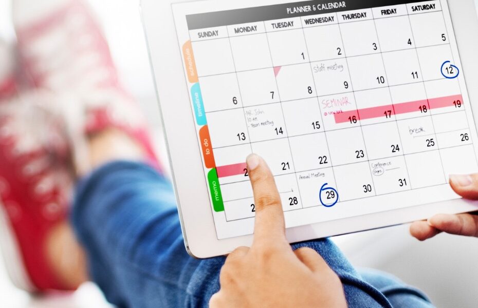 Some one sat with their feet up and they have an ipad with a calendar on it. They are highlighting a section. Part of an article - how to decorate a digital planner like a pro