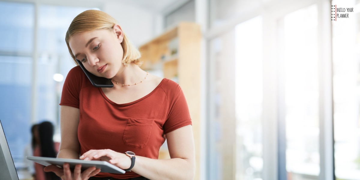 Picture of a woman with a phone to her ear and a tablet in her hands. Part of an article - Make a digital planner: Everything you need to start