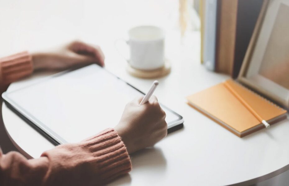 picture of a person sat at a table with an ipad. You don’t see the person or what is on the ipad. they have a Apple Pencil in their right hand. part of an article - a beginner’s guide to digital planning on ipad.