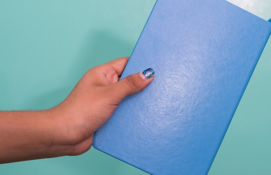Picture of a green background and a woman’s hand is holding a bullet journal. Part of an article - what is a bullet journal spread and how do you make one?