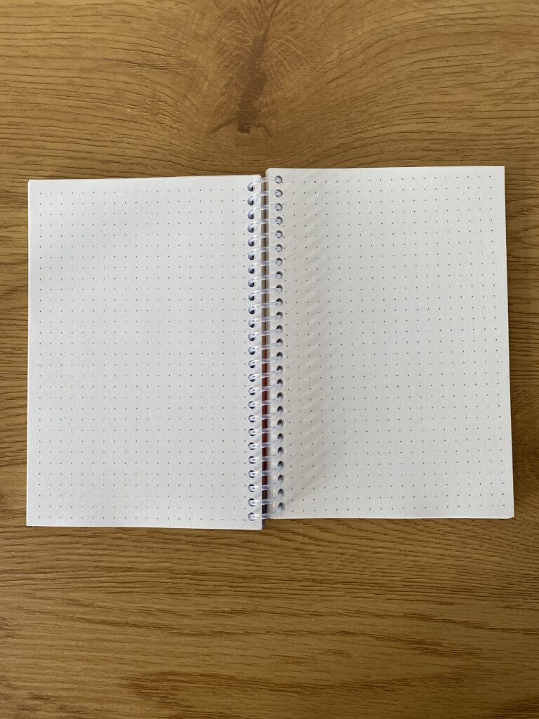 Picture of an open bullet journal notebook using coil spiral binding. Part of an article: Planner Binding Options: Find the Right One for YOU!