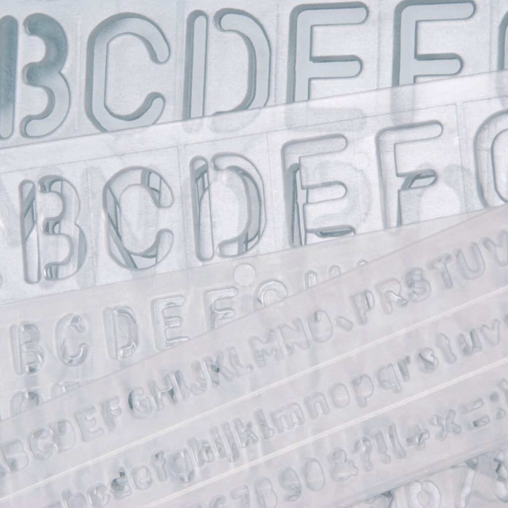 A pile of clear alphabet stencils fill the whole image. Part of an article: Build the Perfect Bujo with these Bullet Journal Supplies for Beginners