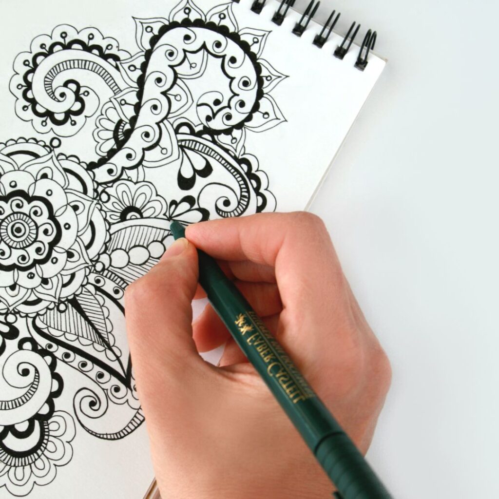A complicated floral drawing with different thickness of pens. A hand is holding a pen to the paper. Part of an article : These Must See Bullet Journal Pens and Markers are Perfect for Beginners
